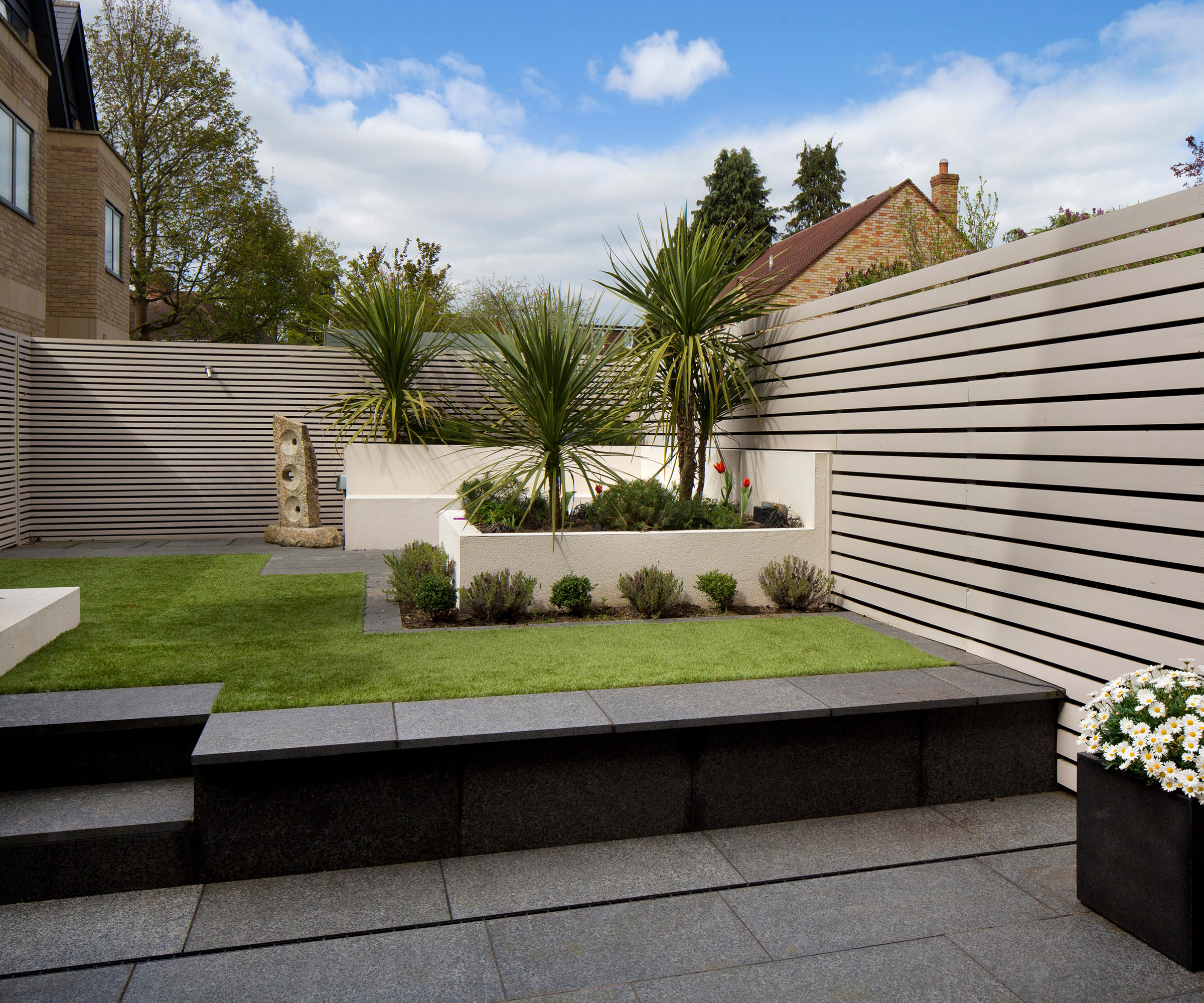 Modern Contemporary English garden with Wooden slated painted screen fence, fake grass and granite paving