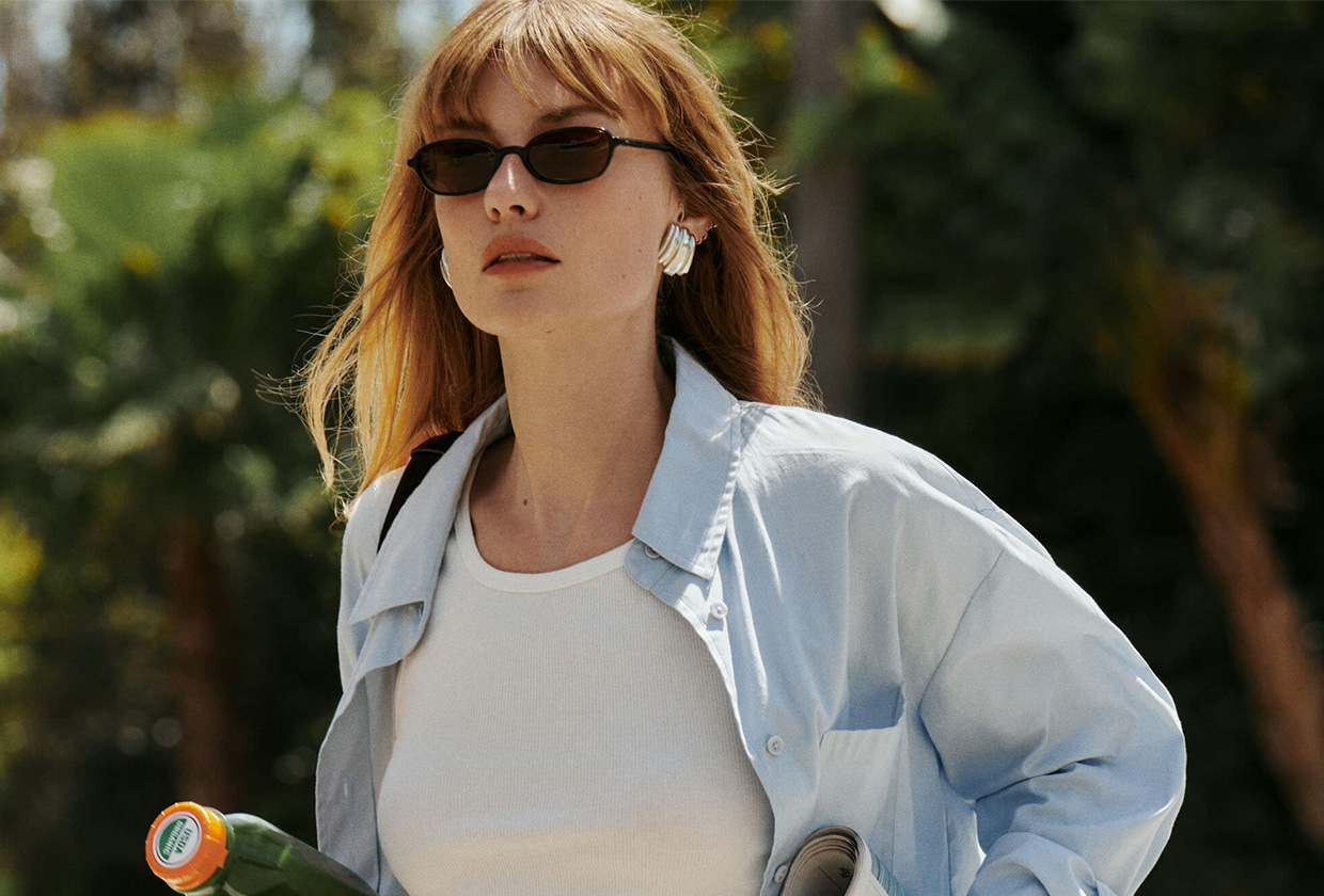 Model wearing the new Reformation x Jimmy Fairly black sunglasses with a button-down shirt and a cropped tank top.