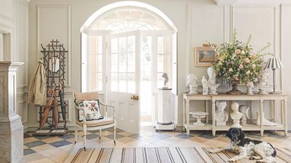 Hallway with arched door, tiled floor, collection of white marble busts and coat rack