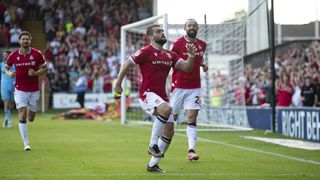 Elliot Lee celebrates a goal for Wrexham in the club&#039;s red shirt and white shorts kit.