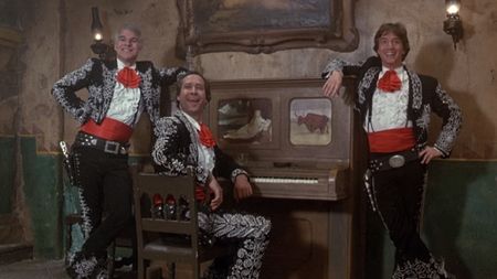 Steve Martin, Chevy Chase and Martin Short smiling by a piano in Three Amigos