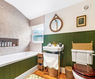 bathroom loft conversion featuring green wall panelling, bath, sink, toilet, window and tiled wall with curved ceiling and recessed shelving