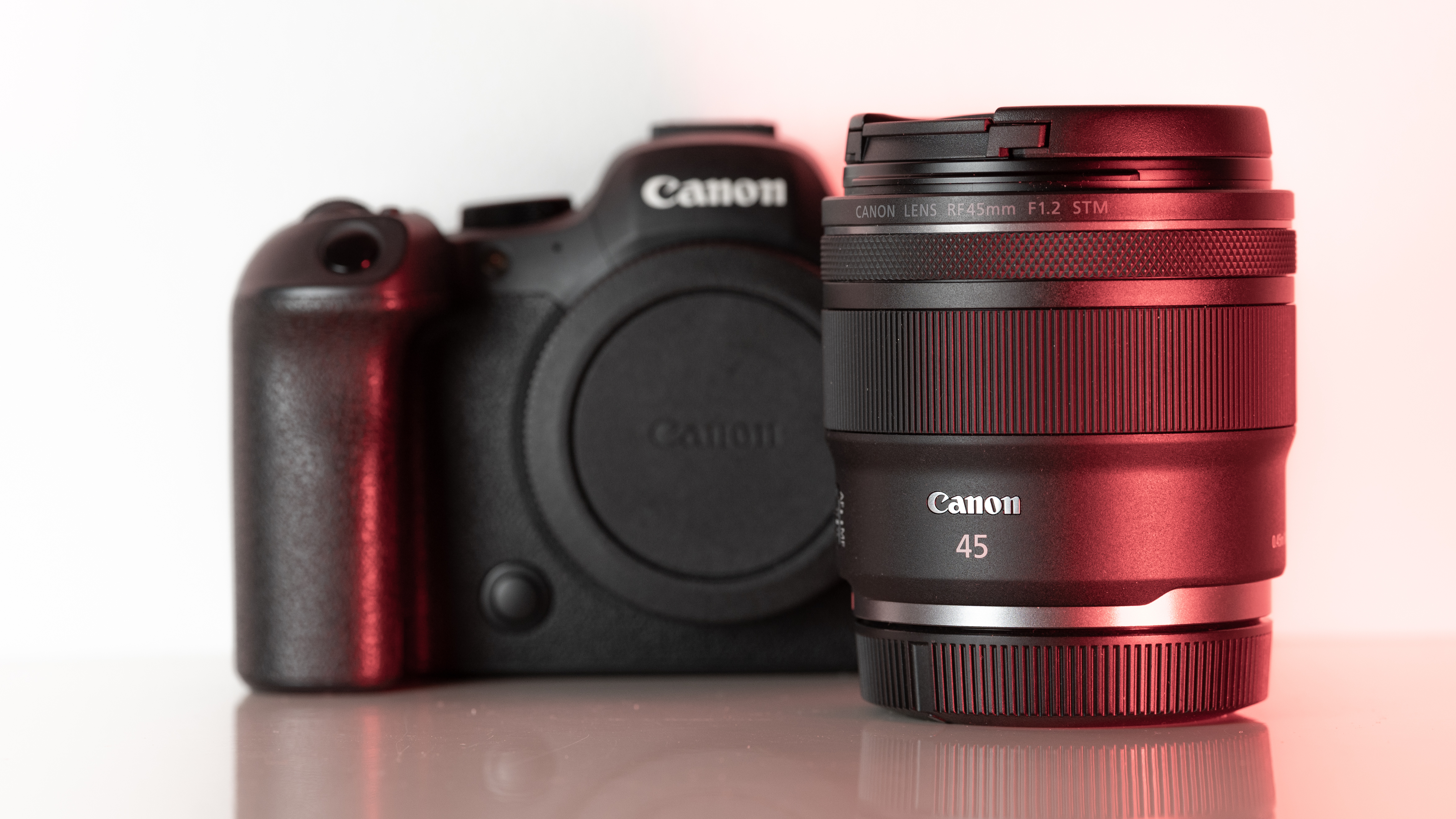 Canon RF 45mm F1.2 STM lens in front of a Canon camera, on a reflective surface, with red lighting