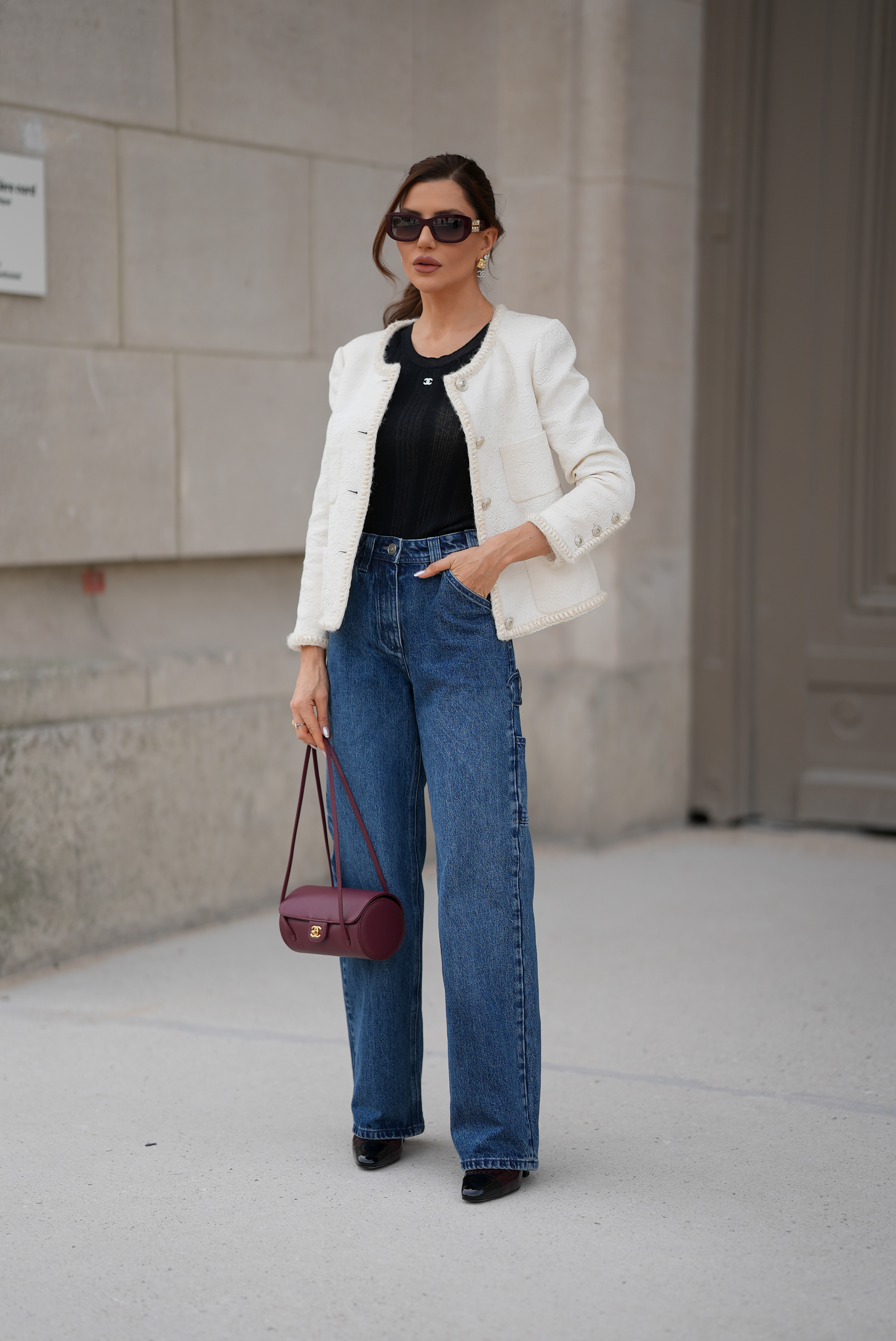 PARIS, FRANCE - JULY 7: A guest is seen wearing a white textured cropped jacket from Chanel with button front and frayed trim; a black ribbed sleeveless top; blue wide leg denim jeans; burgundy and black patent leather pointed toe heels; a small burgundy leather Small Preppy Coco Flap bag from Chanel with cylinder shape, long shoulder straps; gold and pearl earrings; gold rings; rectangular acetate sunglasses from Chanel with dark tinted lenses during Day Two of Paris Fashion Week - Haute Couture Fall/Winter 2026/2027, outside the Chanel show on July 7, 2026 in Paris, France. (Photo by Moritz Scholz/Getty Images)