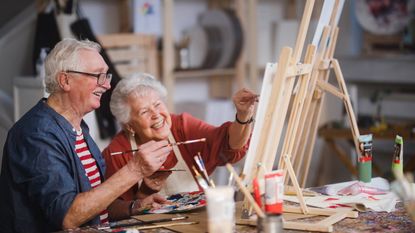 Cheerful elderly couple painting with paintbrushes at art workshop