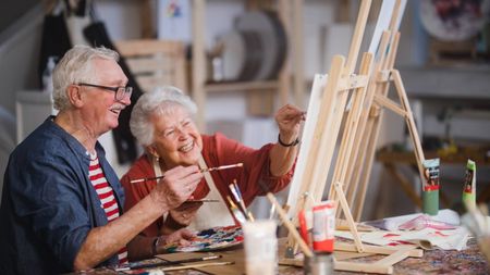 Cheerful elderly couple painting with paintbrushes at art workshop