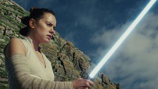 a woman holds a lightsaber and looks at it as though she has never seen such a thing in her life.