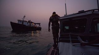 A photograph of an anti-piracy team from the Benin navy checking on a small ship during an evening patrol in the Bight of Benin, off the coast of West Africa. 