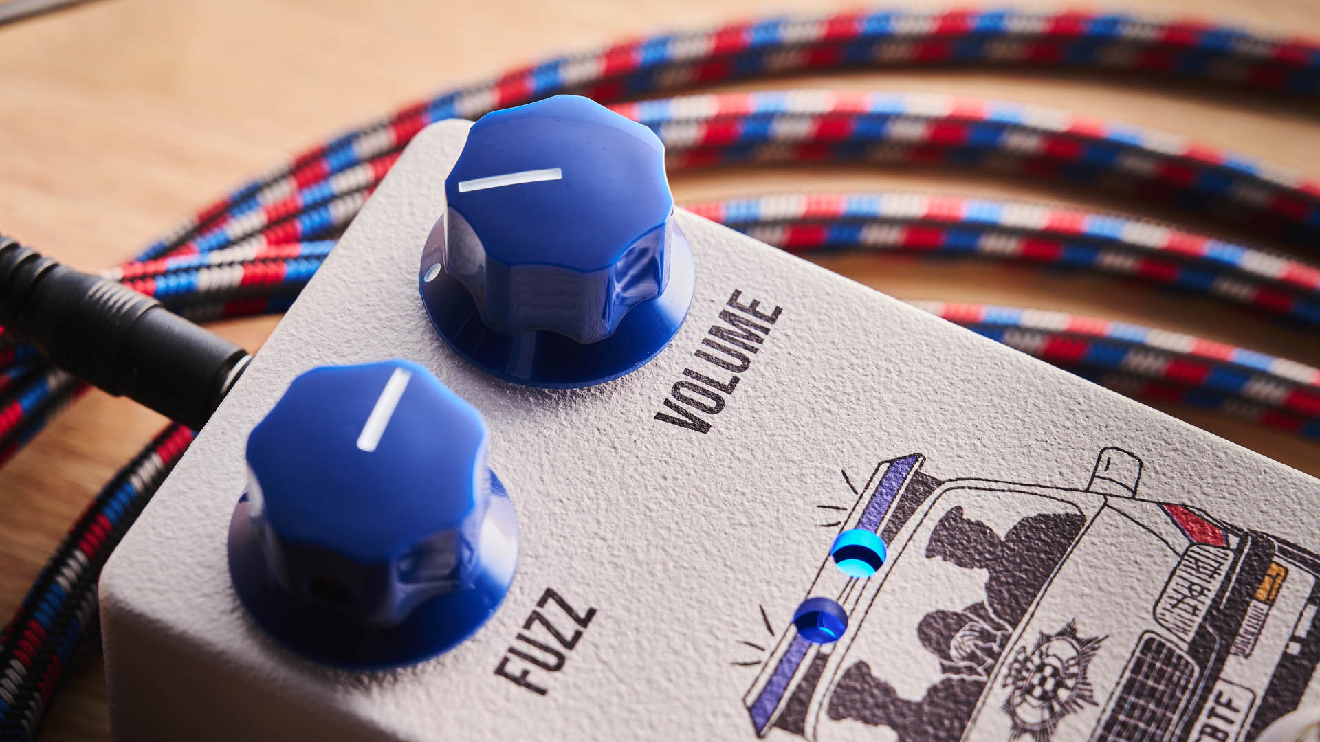 Funny Little Boxes Caught By The Fuzz: inspired by Supergrass, this two-knob fuzz has a white enclosure, blue dials, and a comic graphic of someone being apprehended in a police car.