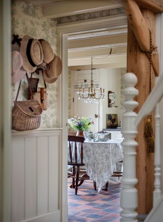 hallway with green toile de Jouy wallpaper straw hats on pegs and view to round table