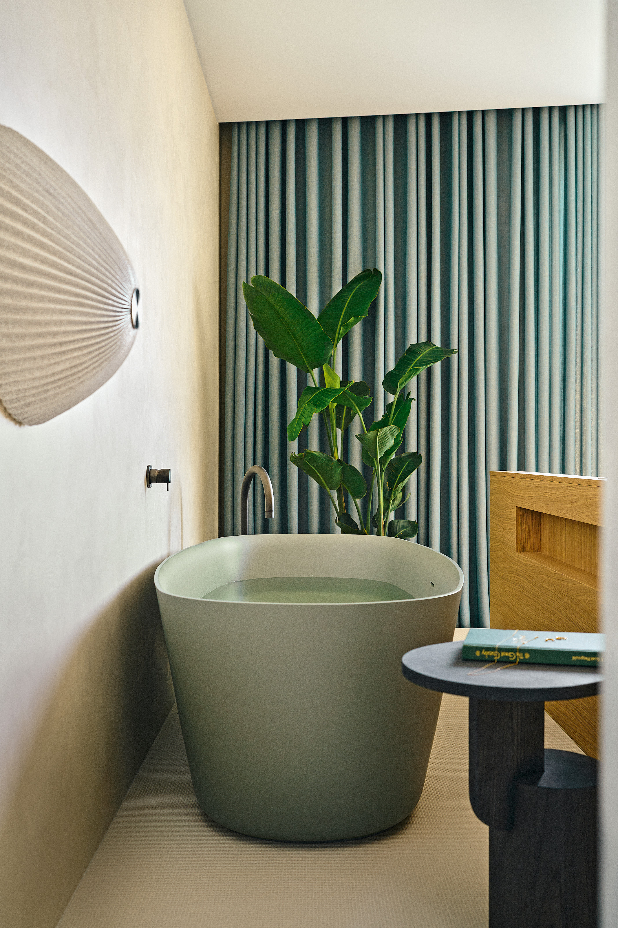 Green freestanding bath tucked behind bed, framed by blue curtains