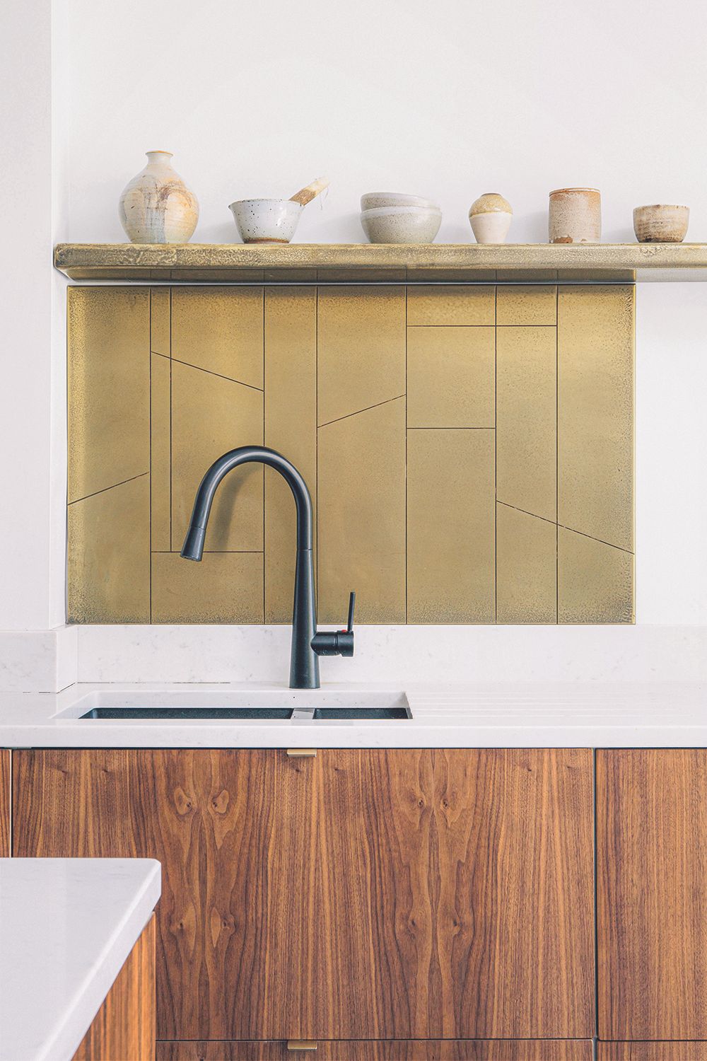 A sink with wooden cabinets, a green backsplash and shelving for decorative ceramics