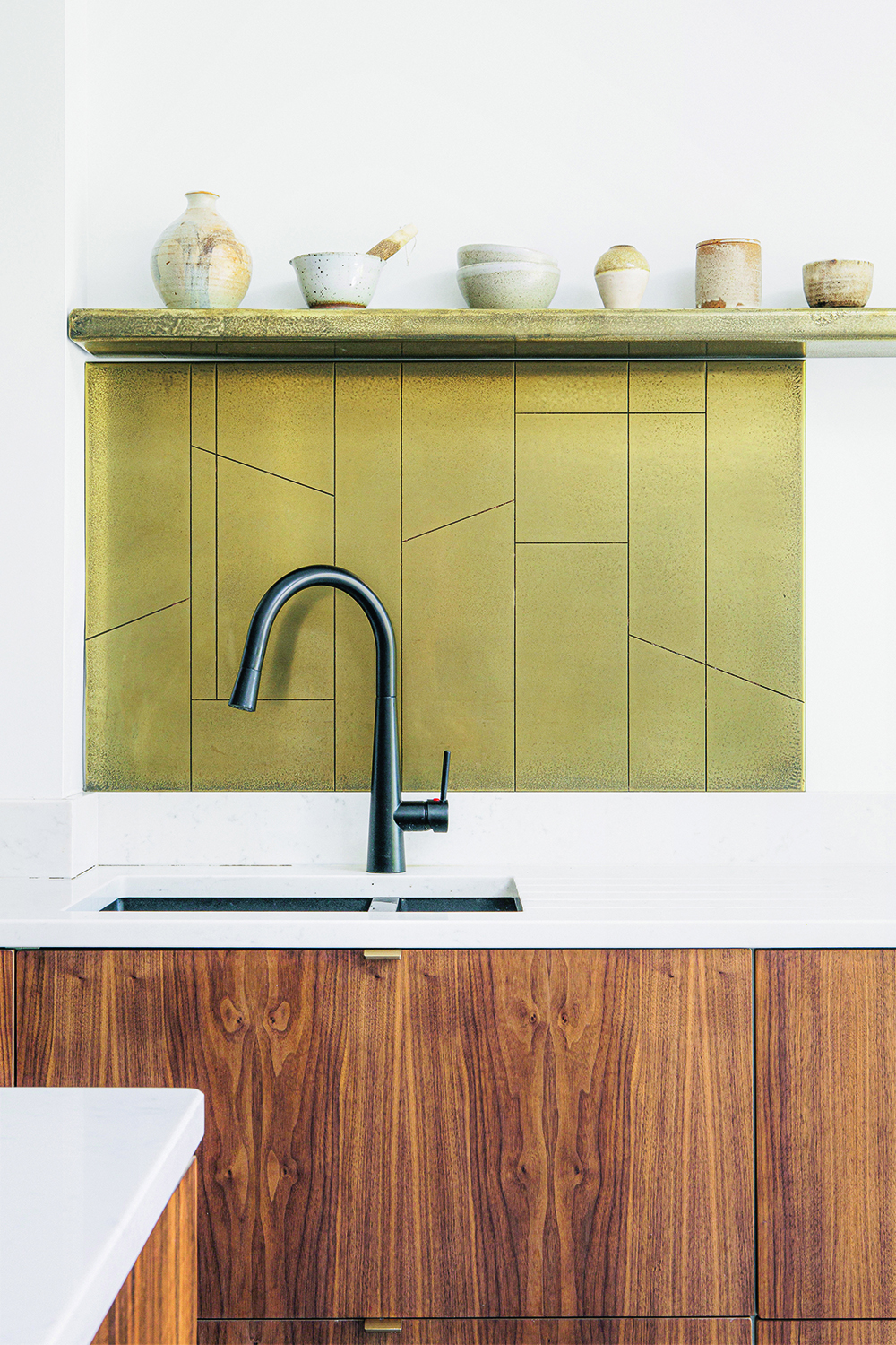 A sink with wooden cabinets, a green backsplash and shelving for decorative ceramics