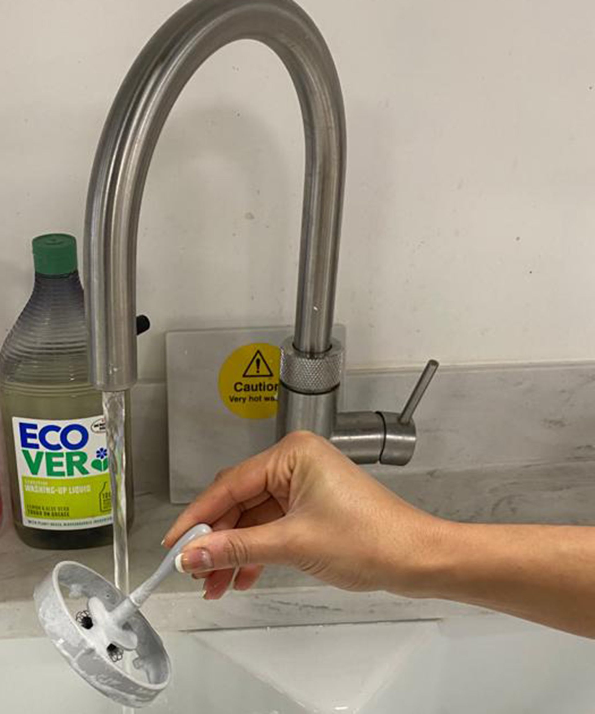 Christina Chrysostomou membersihkan pengocok buih susu Hotel Chocolat Velvetiser di wastafel dengan air mengalir di dapur uji di Reading, Inggris