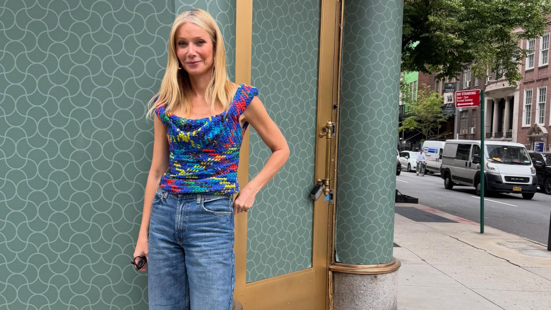 Gwyneth Paltrow poses for a photo wearing blue wide-leg cropped jeans with red heels and a blue top.