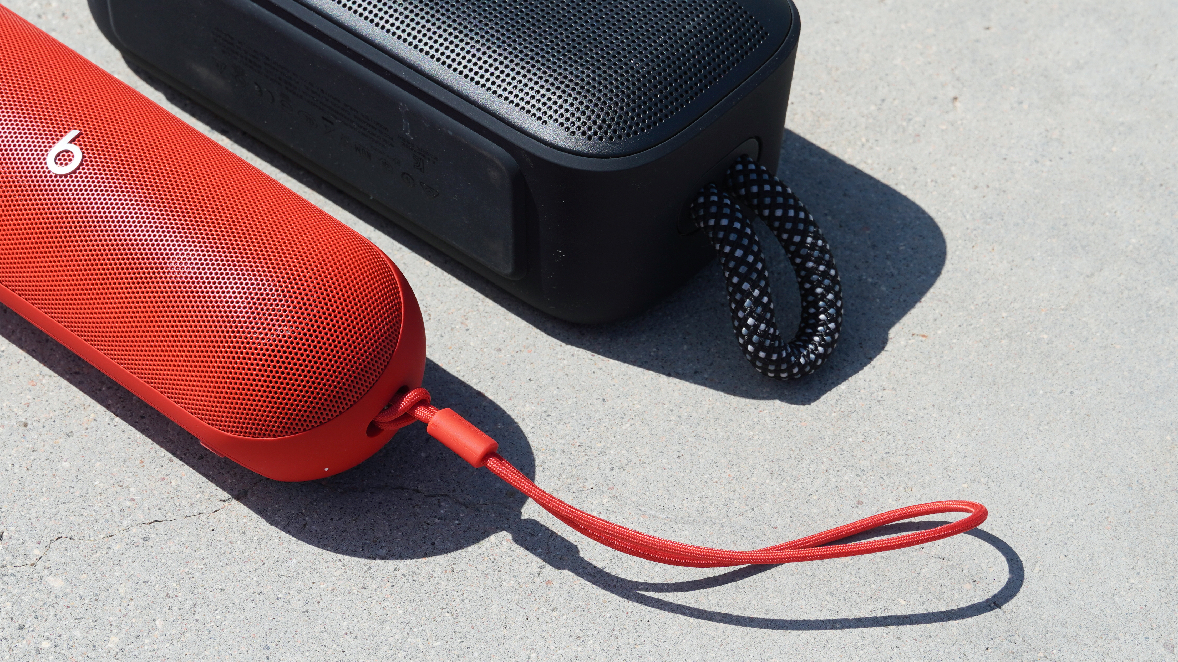 The Bose SoundLink Plus (black) and its utility rope beside the Beats Pill (red) and its lanyard loop.