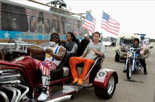Luke Wilson and Terry Crews in the 2006 film Idiocracy. After volunteering for a secret hibernation project, Joe Bauers (Wilson) awakes 500 years in a future where intelligent people have long stopped procreating, making Bauers the most intelligent man on the planet. Here he rides in a motorcade alongside Dwayne Elizondo Mountain Dew Camacho (Crews), the President of the United States.