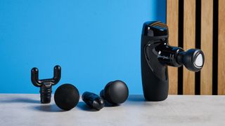 the bob and brad m7 plus mini massage gun in black with 5 attachments including a heat head photographed against a blue background