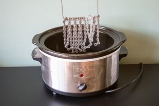 A chain being held on a metal tool over a slow cooker full of wax