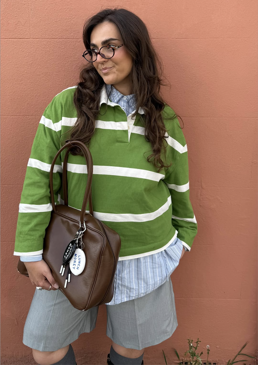 Influencer izabellalily in a green and white striped polo top blue stripped shirt and grey shorts holding a brown bag