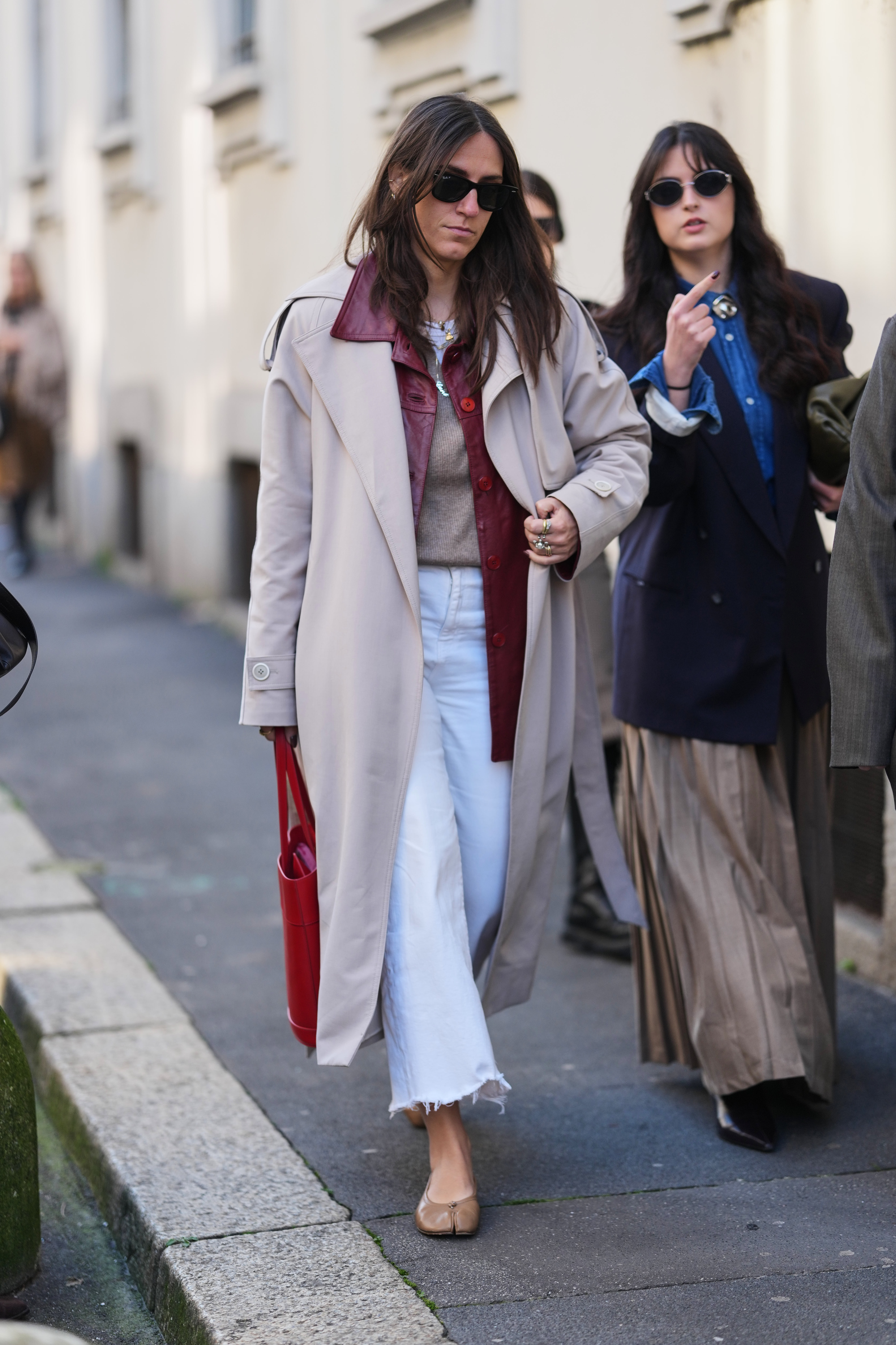 A woman wears frayed-hem jeans with a trench coat and sweater.