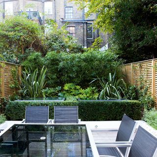 Small garden with dining table and chairs in front of layered plants