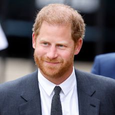 Prince Harry wears a suit and tie and has short red hair and a beard