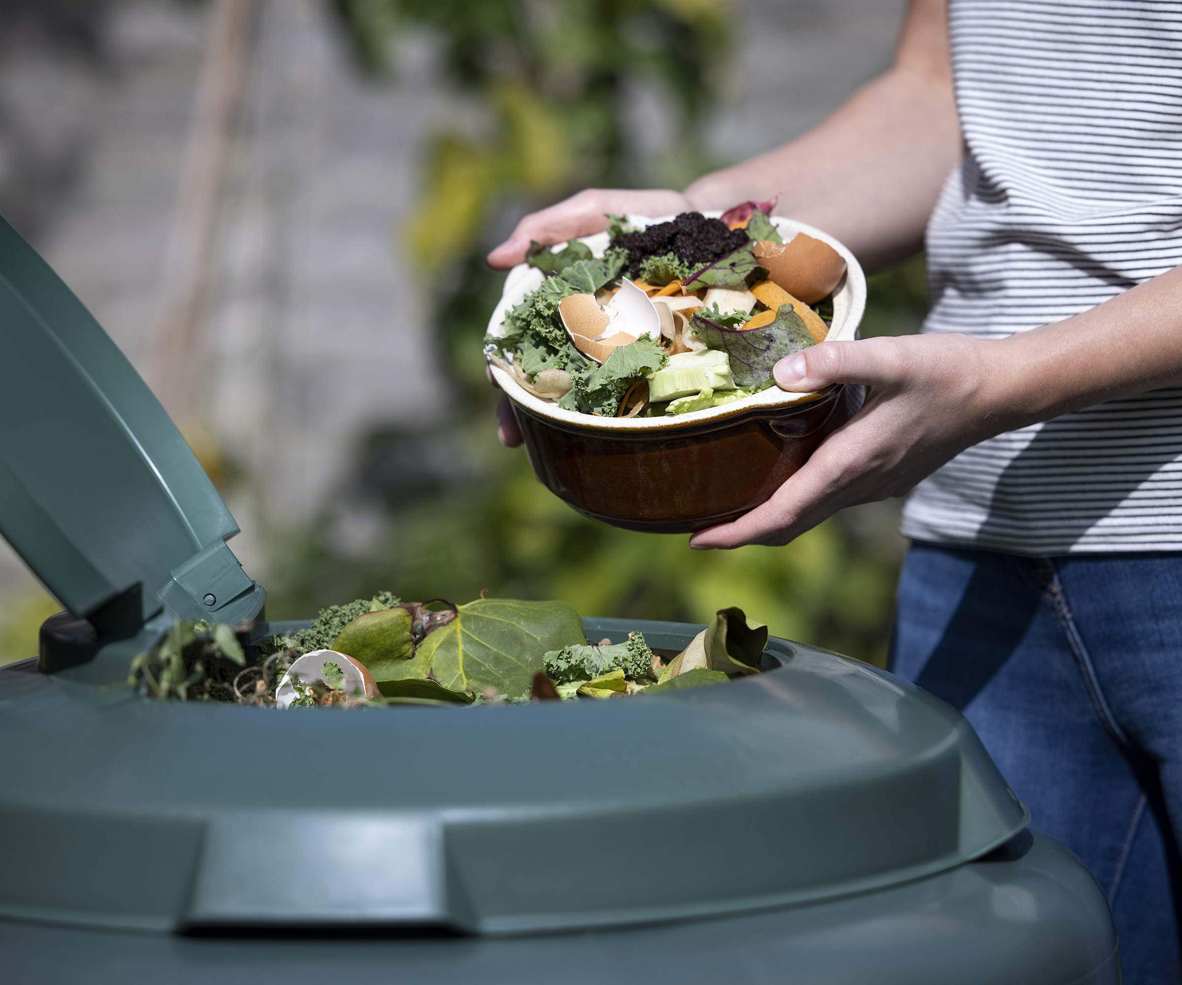 Woman adding kitchen scraps including coffee grounds and eggshells to a compost bin