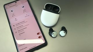 Google Pixel Buds ligger bredvid sitt tillhörande laddningsfodral och en mobil.