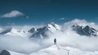 A hiker standing on the top of a snowcapped mountain peak