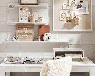 A white desk and white shelves setup in a white dorm room with cute accents like a board and a white fuzzy chair
