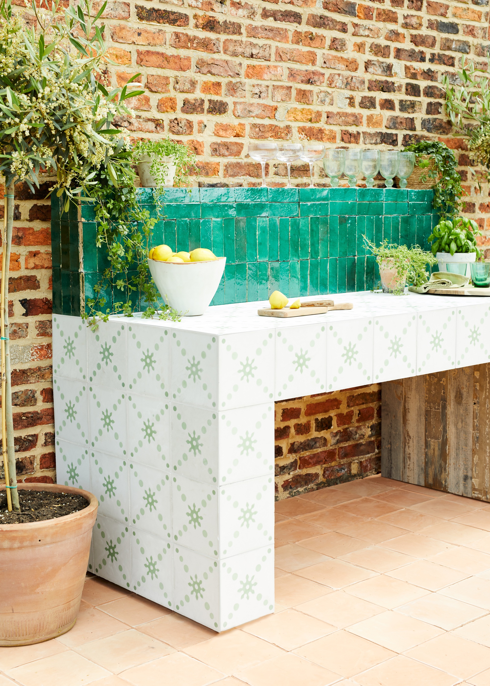 Outdoor kitchen in patterned green tiles with a deep green splashback. There is also a large potted plant placed next to the kitchen counter