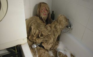 Hairy man holding his dog in the bath