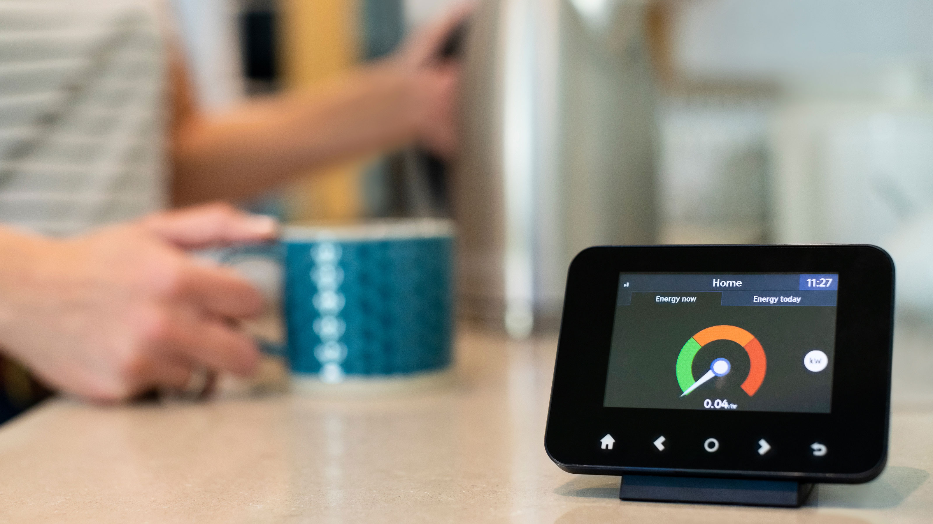 Smart meter on a kitchen bench with a women holding a mug of tea