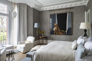grey and pale blue bedroom with grey textured wallpaper, artwork, armchairs, pendants, floor lamps, bay window