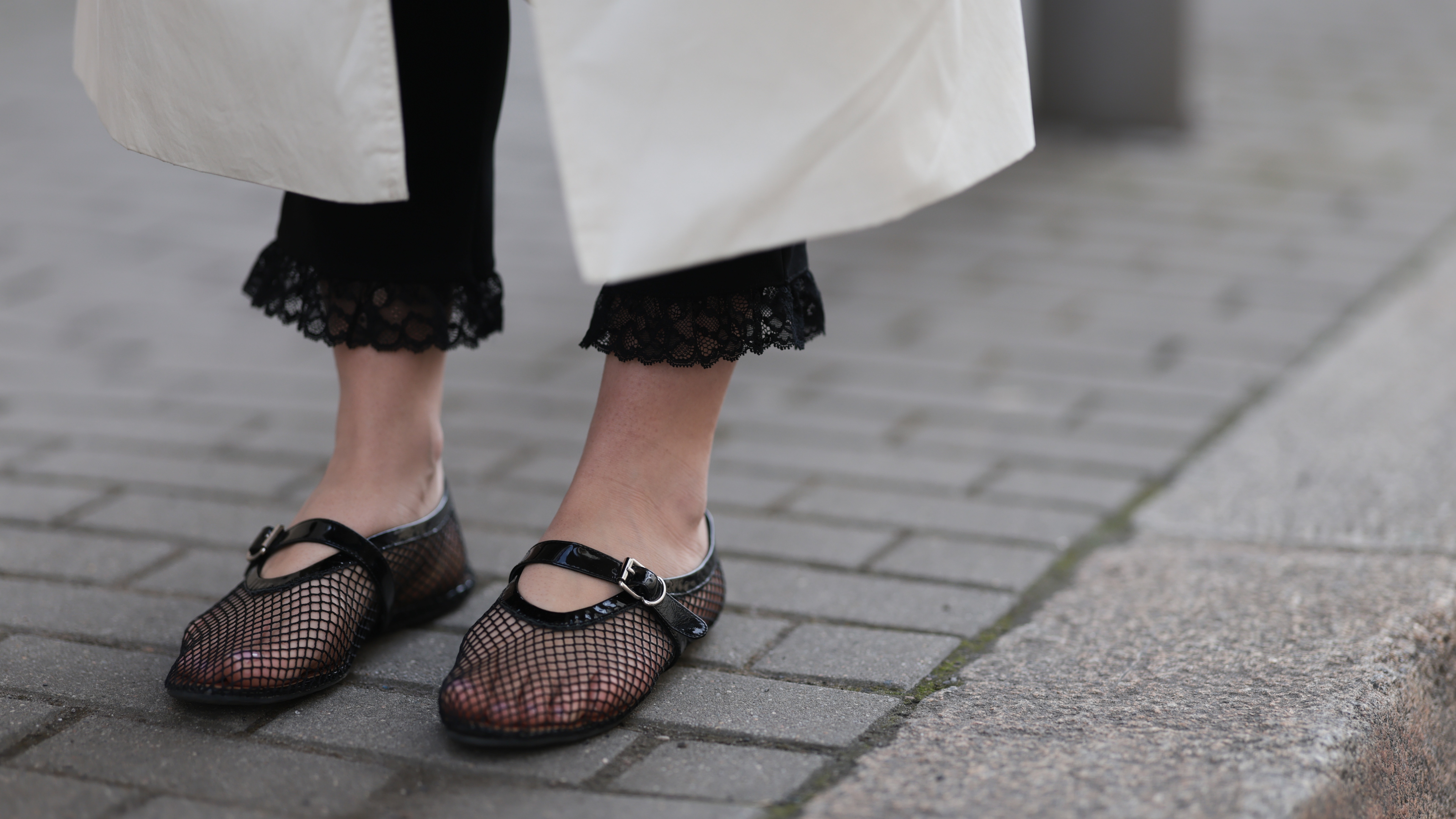 Close-up of black mesh Mary Jane flats styled with lace-trimmed black pants and a white coat.