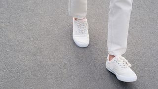 a woman walking in white sneakers on the pavement