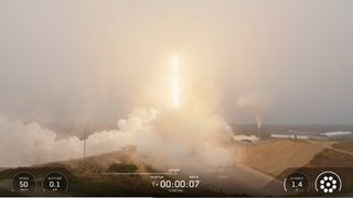 A rocket engine flame is seen peaking through some fog, but only barely.