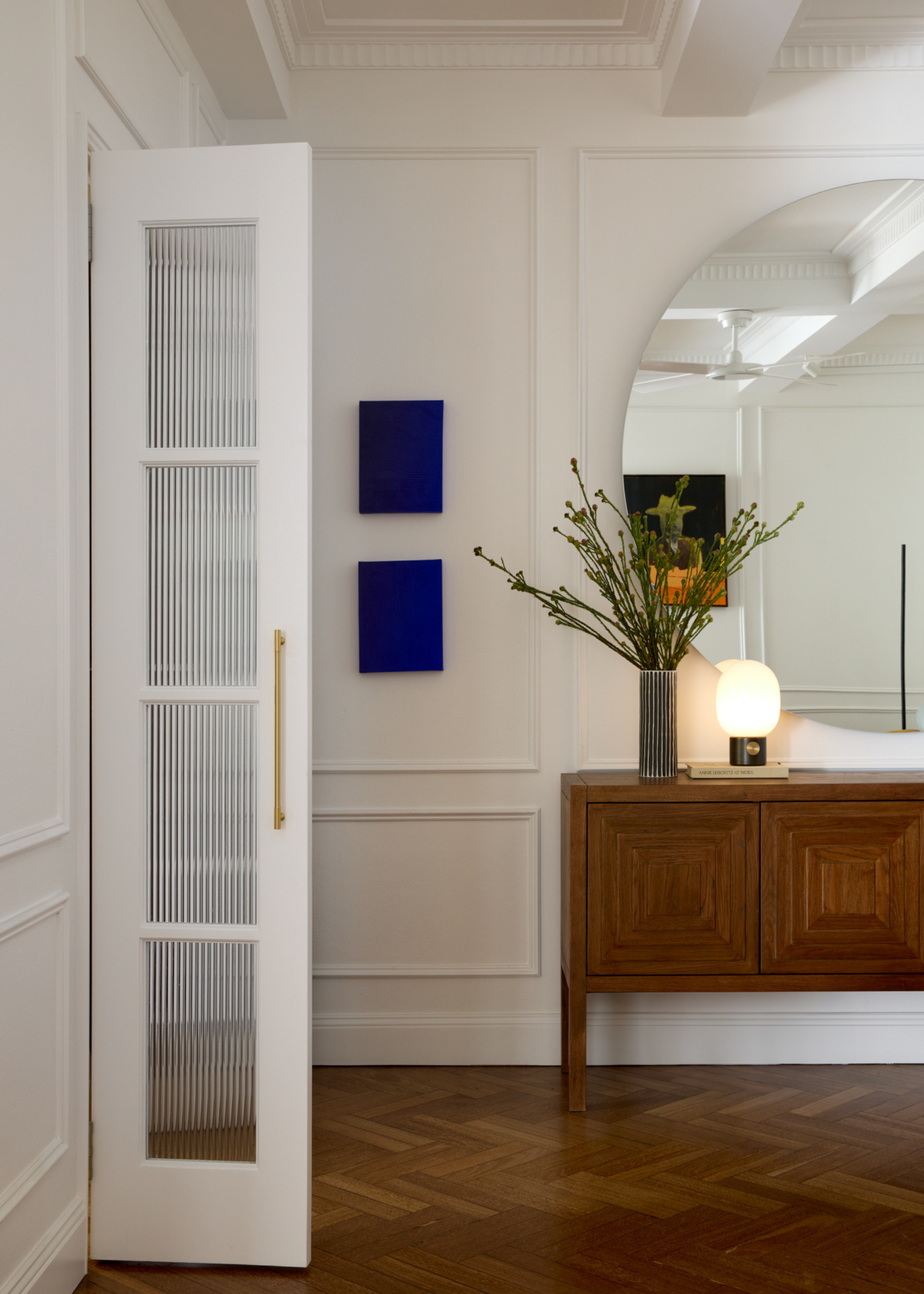 A living room with a round mirror above a wood sideboard