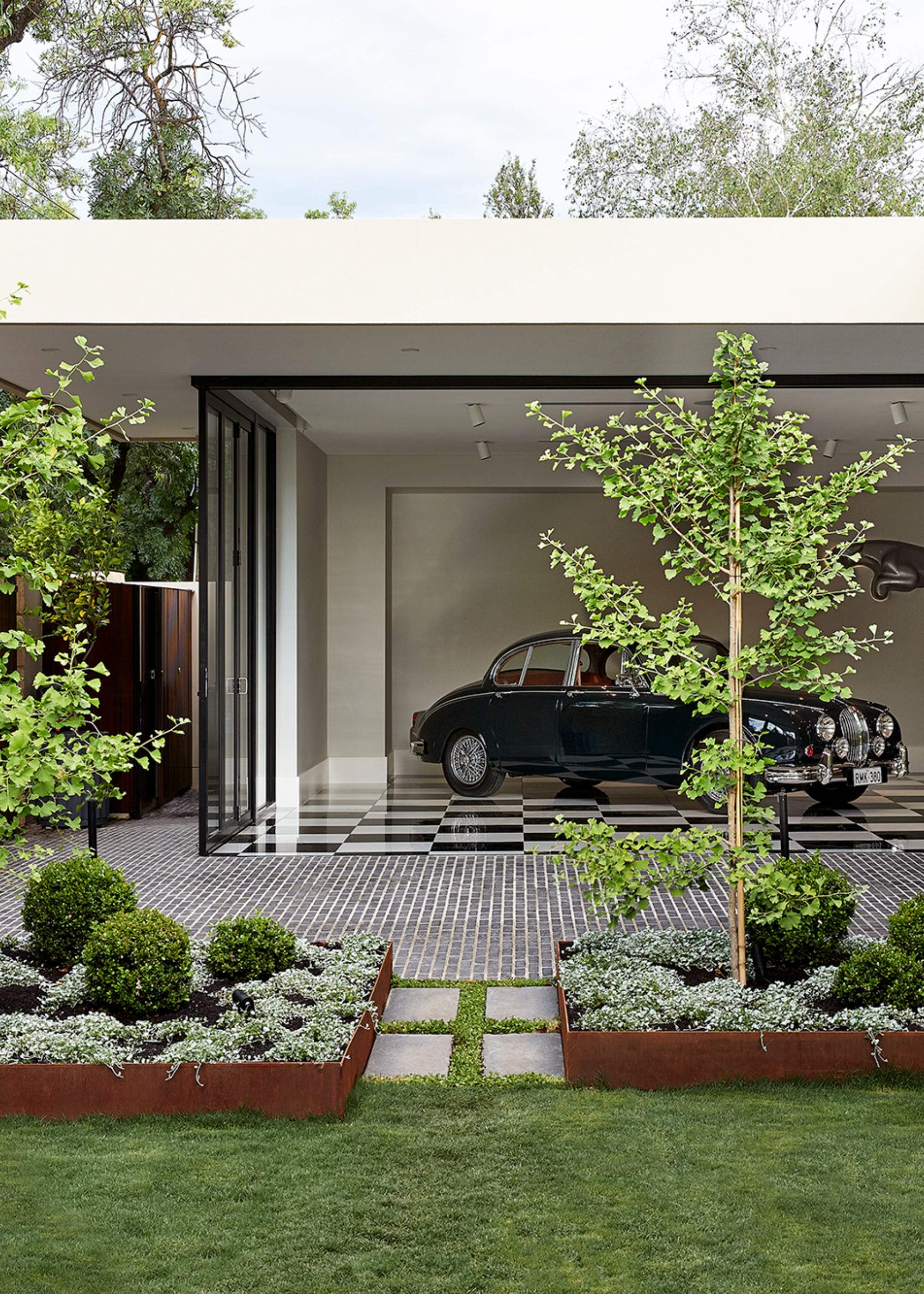A front yard with a stone path leading to a checkerboard floor garage with a vintage car