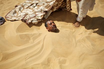 A worker stands next to a patient buried in the hot sand in Siwa, Egypt.