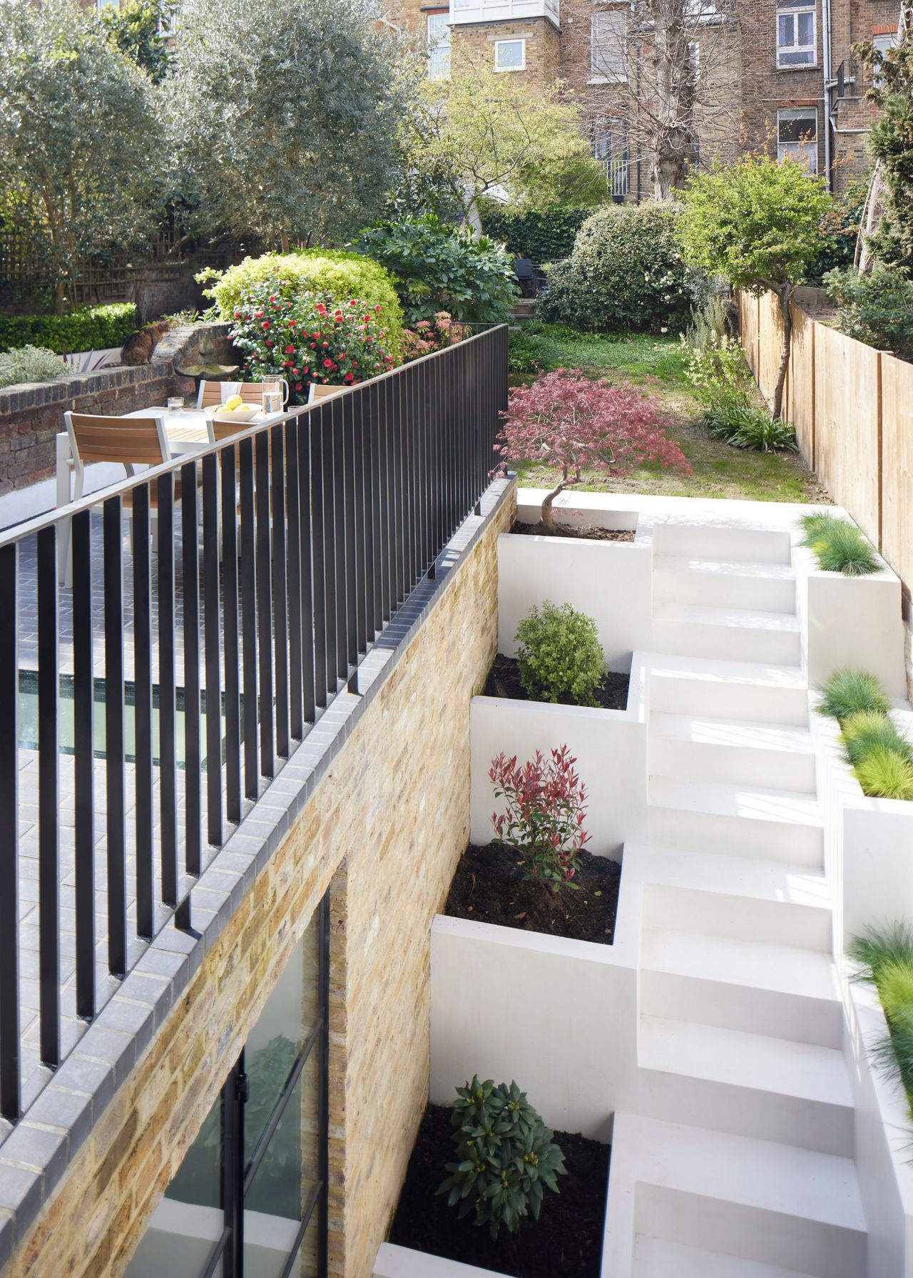 A staircase leading to the upper patio with plants are planted on either side of the white stairs. There is also a view of the upper patio which has a dining table and chairs