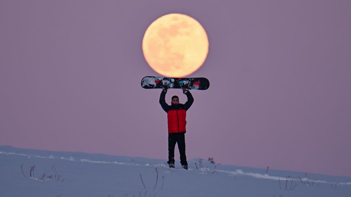 a man with a snowboard poses in front of a full moon