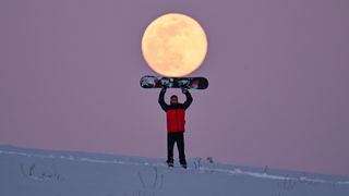 a man with a snowboard poses in front of a full moon