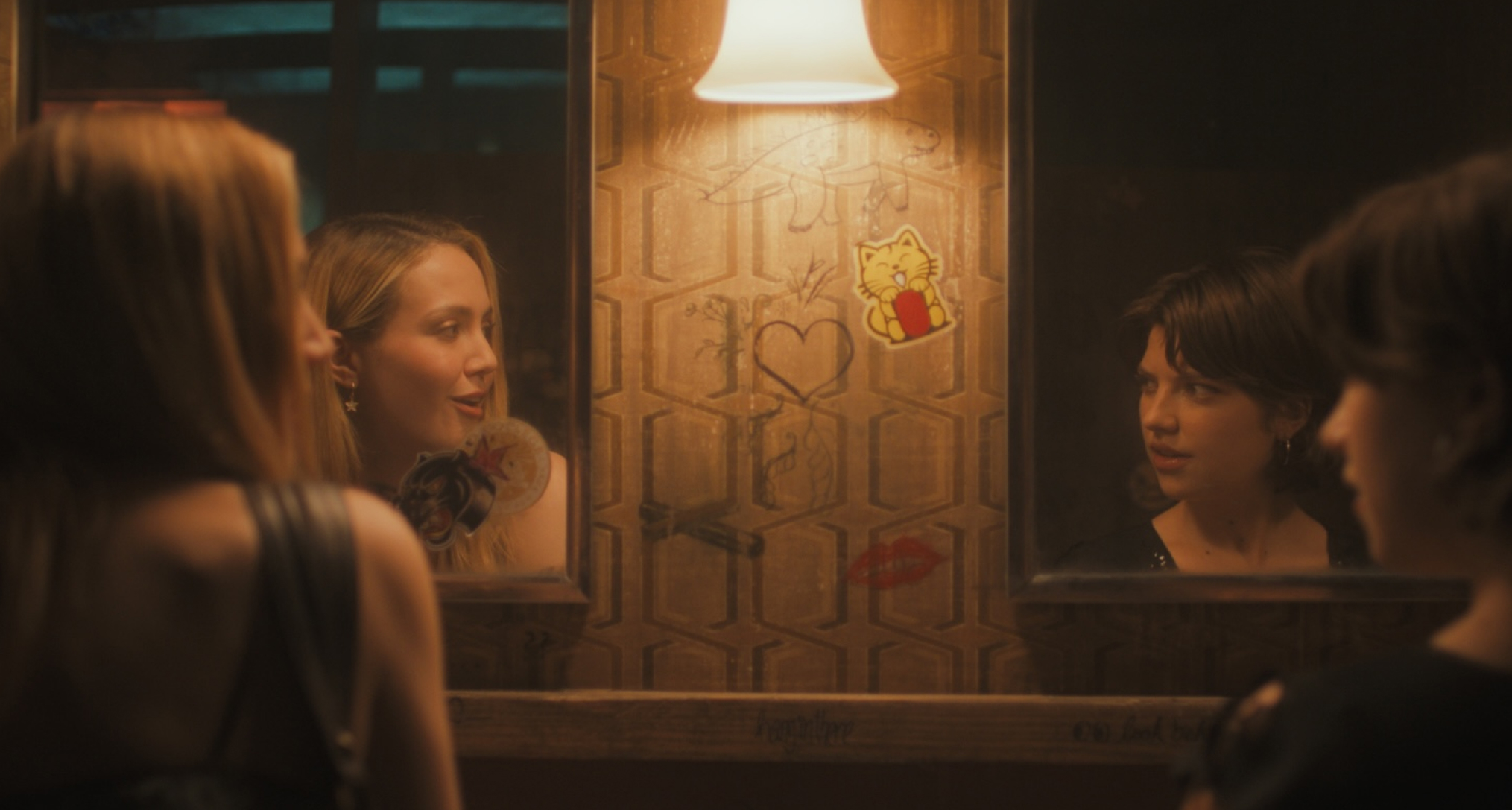 iris apatow as amanda and catherine missal as bree speaking in a bar bathroom with their reflections in a mirror in a still from tell me lies season 3 premiere