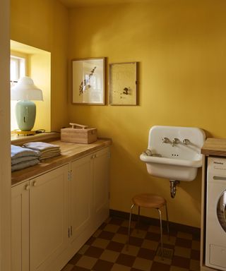 colors experts say to avoid in 2024, small yellow laundry room, with sink, cabinets, checked floor, washing machine, artwork