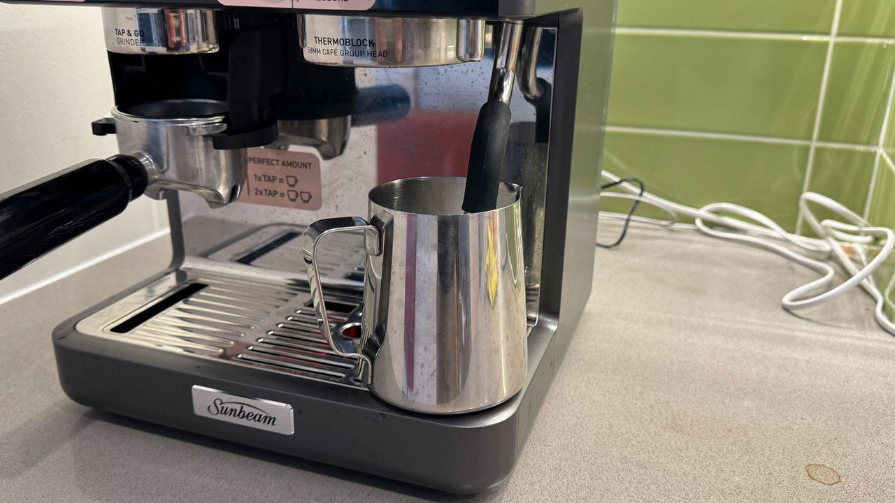 A milk pitcher with the steam wand of the Sunbeam Origins Sense inserted