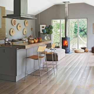 wooden flooring, grey island with wooden worktop, wooden stools, grey walls and log burner