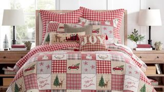 A quilted Christmas bedding set with red plaid and tan patches filled with Christmas design elements with matching pillows made up on a bed.