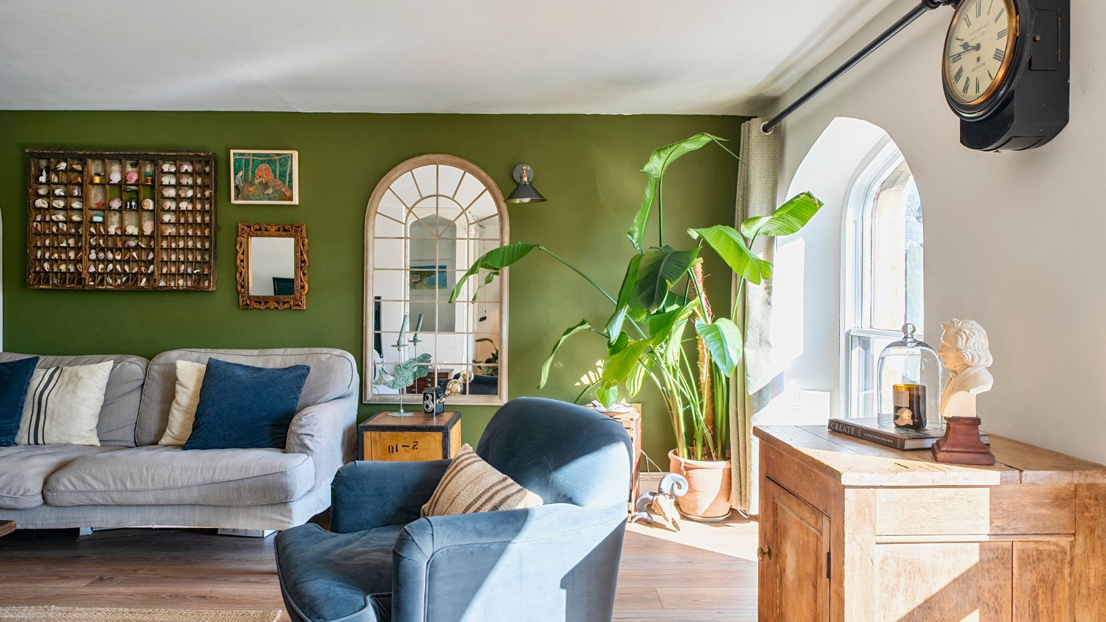 A green living room with arched mirrors, a blue velvet armchair and an antique clock